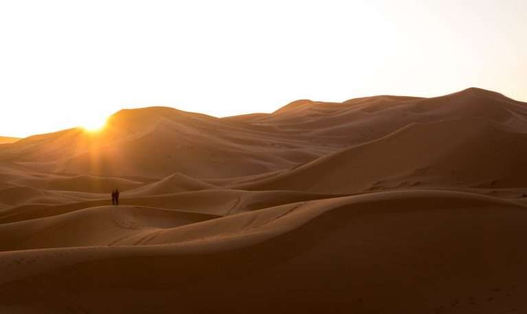 Two people watching the sunset at the Erg Chebbi Dunes in Merzouga, the Sahara Desert, Morocco