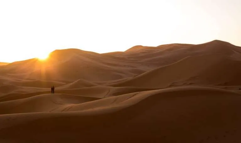 Two people watching the sunset at the Erg Chebbi Dunes in Merzouga, the Sahara Desert, Morocco