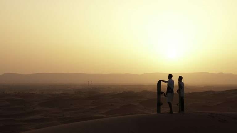 Local sandboarders on the Sahara dunes at sunset