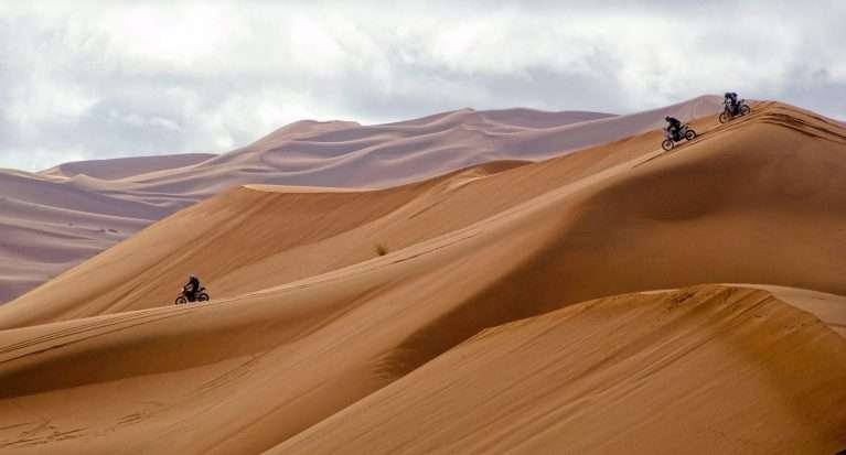 Wind-shaped Sahara sand dunes in Morocco with motorbikes coming down the Erg Chebbi dunes in Merzouga