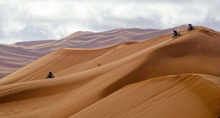 Wind-shaped Sahara sand dunes in Morocco with motorbikes coming down the Erg Chebbi dunes in Merzouga