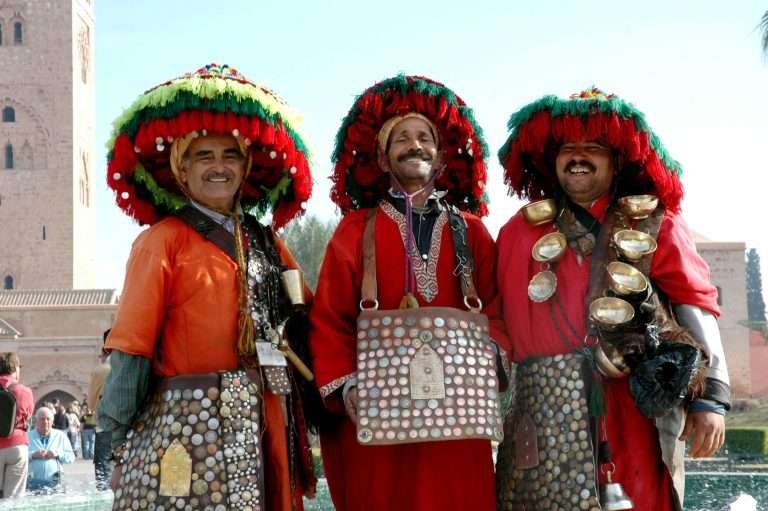 Three men in traditional Moroccan dress and hats posing outdoors at Jemaa el-fna square in Marrakech