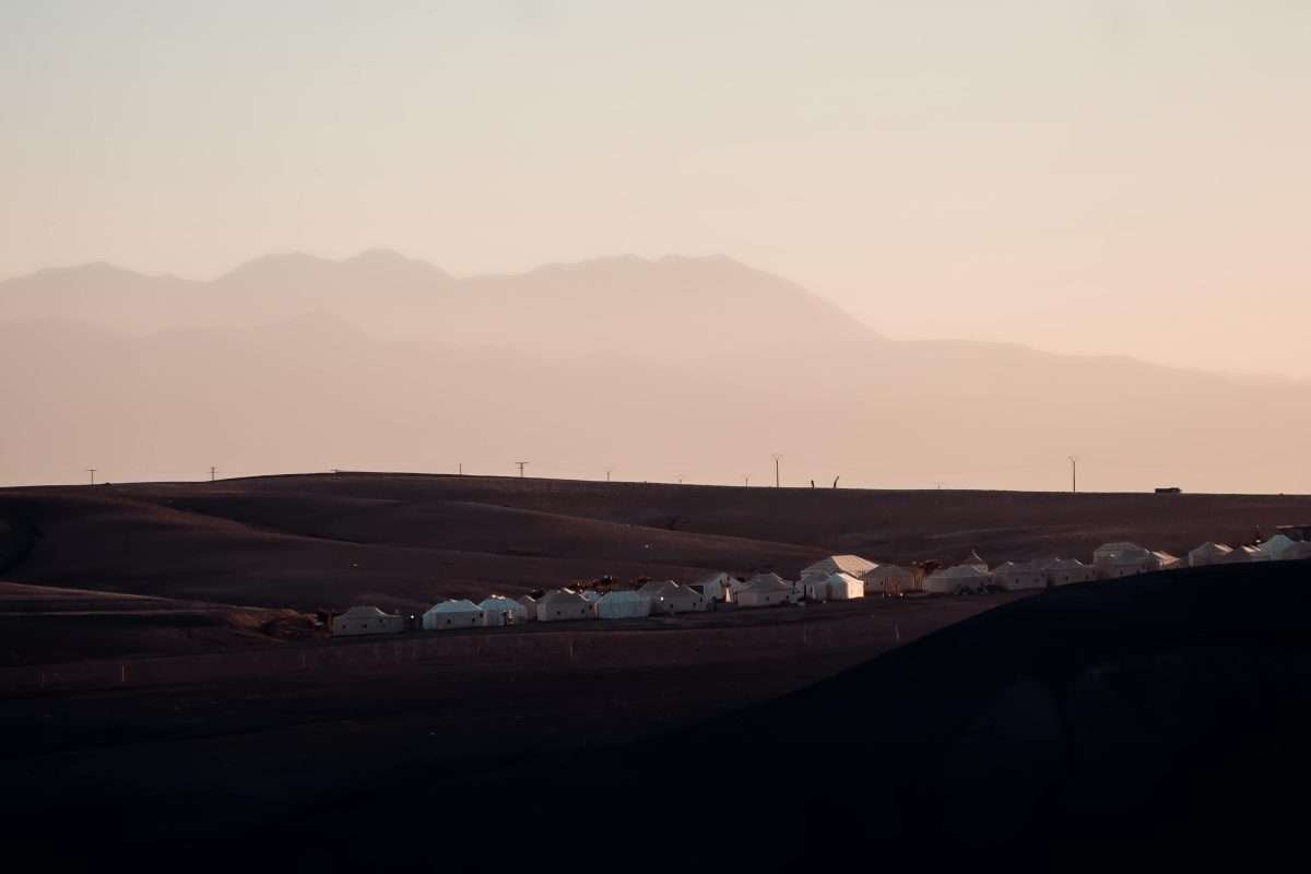 Sunset in Agafay Desert with the Atlas Mountains and a desert camp on the horizon